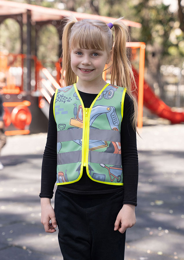 Kind in einer neongrünen Korntex-Warnweste mit Baustellen-Muster auf einem Spielplatz